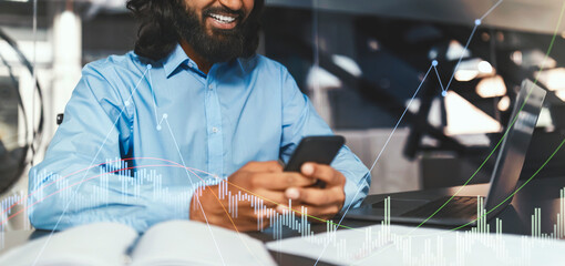 In a modern office space, a professional man with a beard smiles as he checks messages on his smartphone. A laptop and notebook sit nearby, highlighting a productive work environment.