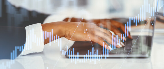In a modern office setting, a Black businesswoman is writing an email on her laptop while analyzing financial data.