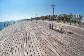 Wooden pier promenade running along coastline with palm trees and buildings in Limassol, Cyprus