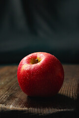 Healthy red apple with fresh water drops on rustic wooden board, representing organic food and natural snack
