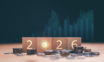 Financial outlook 2026 concept. Wooden blocks displaying the year with target icon and coins, marketing graph in background. Economic forecast, investment planning and future financial strategy.