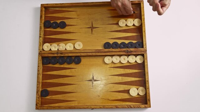 A player's hands engage in a strategic backgammon board game. Rolling dice and moving checkers across the beautiful wooden surface, this video captures the essence of classic leisure and competition.