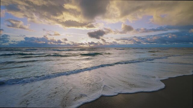 Sunrise waves rolling onto a sandy beach with dramatic golden clouds