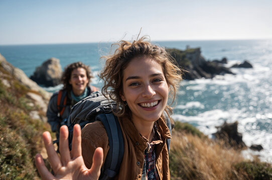Smiling Young Hikers on a Rugged Coastal Trail: Backpackers Taking a Candid Selfie with Ocean Cliffs and Waves