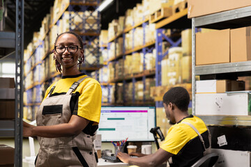 Portrait of happy female worker verifying boxes pallets in e-commerce warehouse. Focusing on...