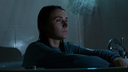 A young woman sits under running shower water at night, overwhelmed and emotionally drained. Dark, cold tones and dramatic lighting reflect sadness, stress, and mental struggle. 