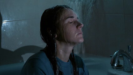 A young woman sits under running shower water at night, overwhelmed and emotionally drained. Dark, cold tones and dramatic lighting reflect sadness, stress, and mental struggle. 