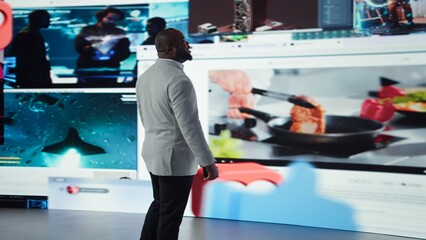 Man browsing social media feed on smartphone in front of digital video wall. Person using phone with thumbs up and heart icons floating behind him, highlighting interactive engagement online, camera A