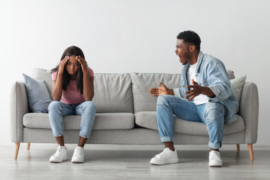 Relationship Problems Concept. Emotional annoyed stressed black couple arguing at home sitting on couch. Angry irritated nervous guy shouting at shocked and frustrated gaslighted lady, fighting - Powered by Adobe