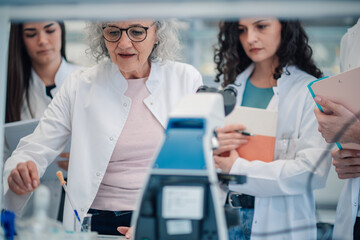 Senior scientist teaching students in lab using microscope