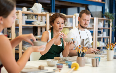 Three students in pottery workshop learn to create homemade plates and other utensils from clay