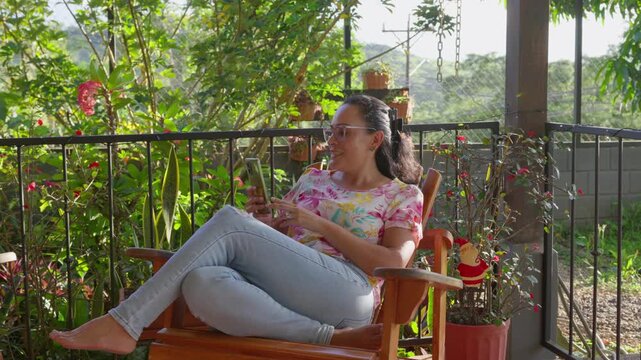 Latina woman smiling at phone while relaxing in warm sunset light on home porch