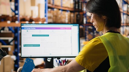 Asian employee typing tracking info from airway bill labels before shipping parcels, managing the order fulfillment process in industrial storehouse. Large business depot with packages Camera B.