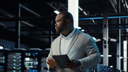 Server room admin doing troubleshooting to prevent downtime. IT specialist in data center reviewing reports and files, crosschecking network performance metrics and security logs, camera B