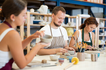Three students in pottery workshop learn to create homemade plates and other utensils from clay