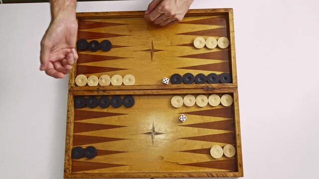 Engaging in a strategic backgammon game, featuring a person rolling dice and moving checkers on a vintage wooden board against a clean white background.