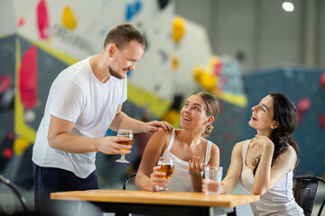 Young man approached to meet two young women sitting at table on climbing wall