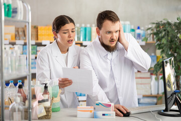 Obraz premium Man and a woman pharmacists work in pharmacy, they are puzzled by the lack of goods and an error in the computer system.
