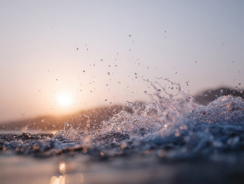 Water splash with sun setting in background creating soft warm light and sparkling droplets on surface of sea