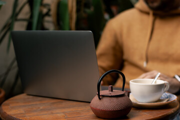 Man Working on Laptop in Cafe Garden While Enjoying Tea