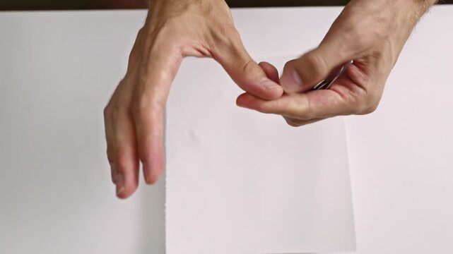 Close-up view of a person using a silver nail clipper to precisely cut their fingernails on a clean white surface. Emphasizes personal care, health, and a meticulous grooming routine.