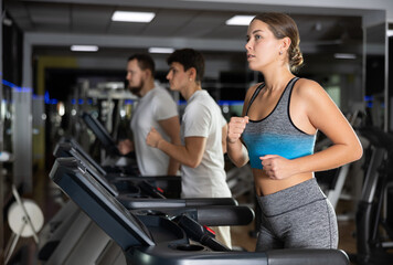 Fototapeta premium Woman runs on a treadmill in the gym. European woman performs cardio zone training