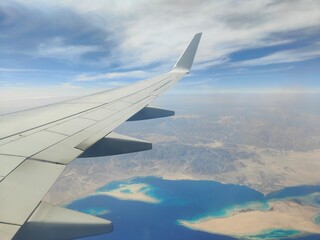 Aerial View of Airplane Wing Over Coastline and Sea, Red Sea, Egypt - A high-resolution aerial photograph taken from an airplane window, showing the aircraft wing above a deep blue sea with a desert c