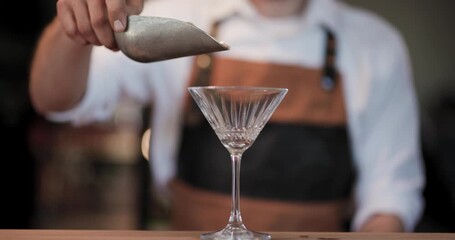 Expert bartender carefully adds ice to a martini glass, highlighting mixology and cocktail artistry in slow motion.