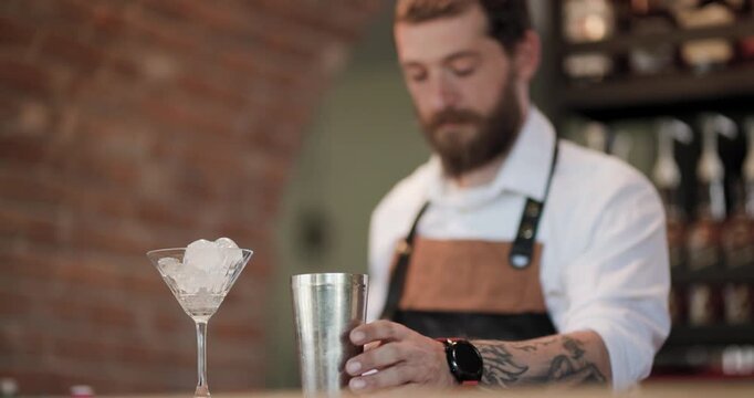 Barman prepares a cocktail with ice and shaker at a bar in the evening hours