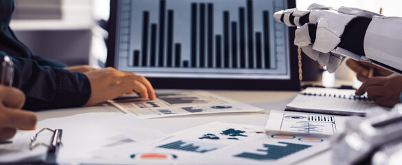 A collaborative workspace scene featuring human hands and a robotic arm working together to analyze various data charts and graphs, symbolizing technology and teamwork.Noogenesis
