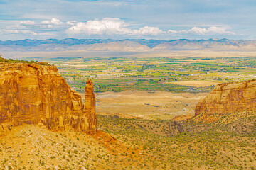 Dramatic red sandstone canyon overlooking a desert valley and distant plains at Colorado National Monument.