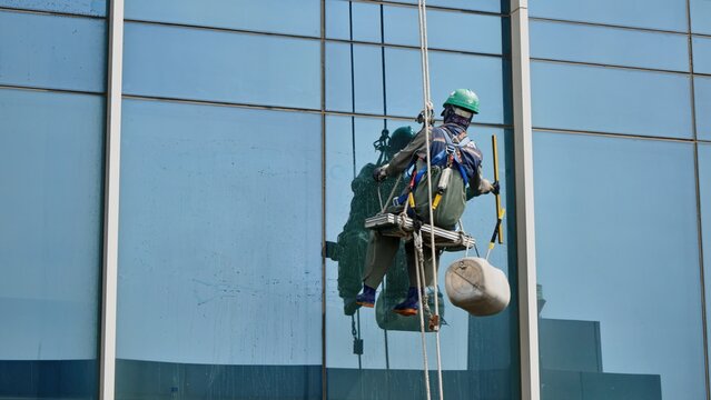 Worker Cleaning Windows On A Modern Glass Skyscraper Building Exterior