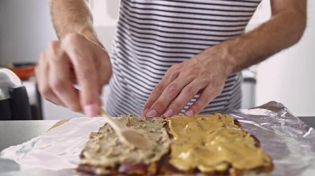 A person meticulously spreads creamy nut butter on a base, then expertly drizzles melted chocolate, creating a tempting homemade dessert or sweet treat ready to be enjoyed.