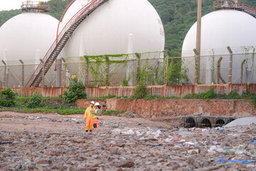 Two environmental specialists in safety gear conduct a field investigation at a polluted coastal site, collecting data and assessing contamination risks near an industrial zone.