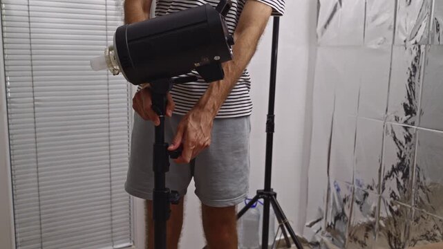A person's hands carefully adjust a professional studio strobe light on a tripod.