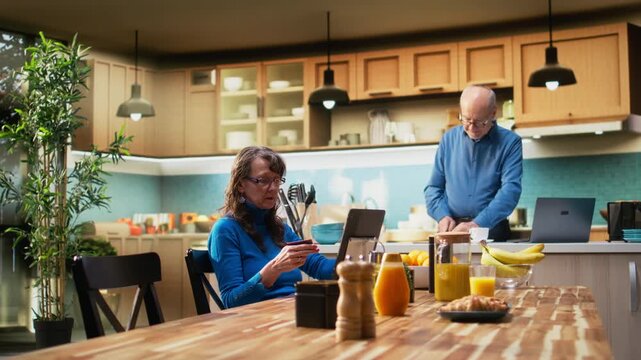 Elderly woman doing online shopping with a credit card in hand, reviewing list of groceries and daily essentials in e-commerce app cart on laptop. Shopper checks credentials for order. Camera A.