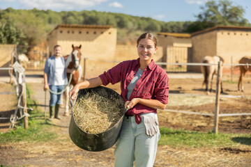 Young woman holding bucket of hay feed for horse in paddock © JackF