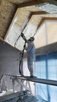 Professional worker spraying polyurethane foam insulation on ceiling