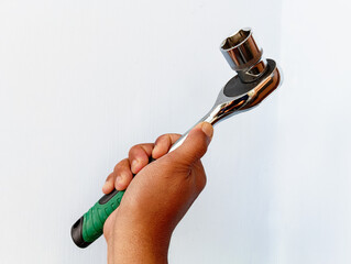 A closeup shot of a hand holding a ratchet wrench with a socket attached, shown against a clean white background, highlighting a simple, functional, and durable mechanical tool.