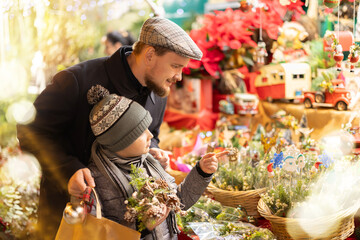 At Christmas market, dad and son look at bouquets and ikebanas made up of twigs of spruce, pine,...