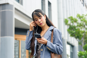 Business woman person enjoying urban lifestyle work travel commute outdoor street scene, listening music with earphones smartphone walking city urban street with modern architecture