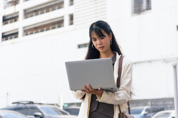 Fototapeta premium Travel woman people person lifestyle street business work outdoor young Asian executive intently uses portable laptop computer managing digital tasks on modern city near tall corporate building