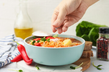 Woman salting delicious lentil soup at light grey table, closeup