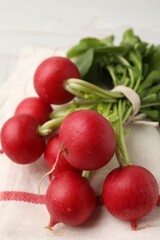 Bunch of fresh radishes with green leaves and napkin on light table, closeup