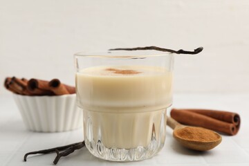Delicious protein shake in glass, cinnamon and vanilla pods on grey table, closeup
