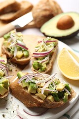 Delicious bruschettas with avocado, onion and microgreens served on light table, closeup