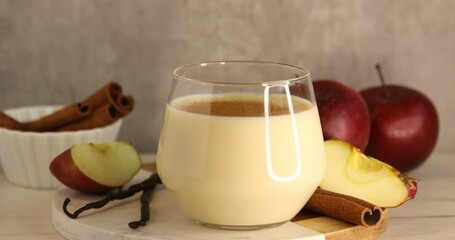 Sprinkling cinnamon onto delicious protein shake, vanilla pods and apples at table, closeup