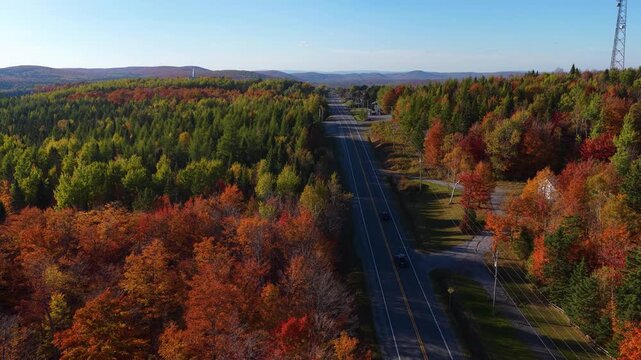 Aerial autumn view of a rural road near Stornoway in the Eastern Townships, Estrie, Quebec, Canada. Colorful fall forest and warm falling sun creating a scenic seasonal landscape.