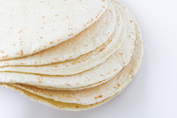 Closeup view of a stack of tortilla wraps placed on a clean white background, highlighting their soft texture and light, speckled surface.