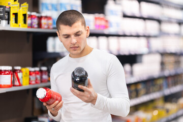 Focused young guy choosing a bottle of vitamin supplements in large sports nutrition store